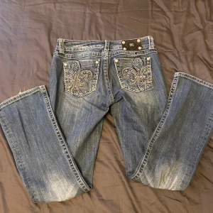 Miss Me blå bootcut jeans med broderi - Snygga blå jeans från Miss Me i bootcut-modell med broderade bakfickor och nitar. Jeansen har kontrastsömmar, klassisk femficksdesign och coolt broderi med stenar på bakfickorna. Modellen heter Easy Boot och är i mjukt jeanstyg. Väldigt fin passform. Tyvärr för stora för mig.