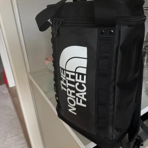 Svart ryggsäck från The North Face - Säljer en svart ryggsäck från The North Face med stor vit logga på framsidan. Väskan har rejäla axelremmar, dragkedja upptill och är tillverkad i slitstark syntet. Perfekt för dig som vill ha en cool och praktisk väska till vardagen.