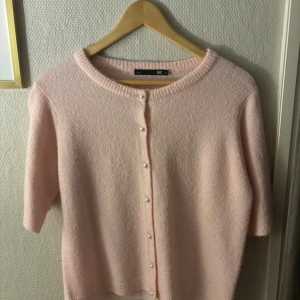 Ljusrosa kofta från 157 med pärlknappar - Supersöt ljusrosa kofta från 157 med korta ärmar och rund halsringning. Koftan har pärlknappar framtill och är stickad i ett mjukt material som känns fluffigt. Perfekt för dig som gillar en söt och feminin stil. Använd ca 2-3 gånger. Vill du ha bilder med tröjan på så är det bara att skriva🫶🏻