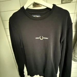 Svart Fred Perry sweatshirt S - Svart sweatshirt från Fred Perry i storlek S. Tröjan har rund hals, ribbade muddar och ett broderat Fred Perry-logo på bröstet. Stilren och enkel design som funkar till många olika looks. Materialet känns mjukt och skönt mot huden.