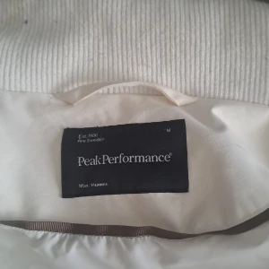 Vit bomberjacka från Peak Performance - Snygg vit bomberjacka från Peak Performance med ribbade muddar och krage. Jackan har dragkedja framtill, diskret logga på bröstet och praktiska fickor. Materialet är mjukt och känns sportigt, perfekt för dig som gillar stilren och clean look.