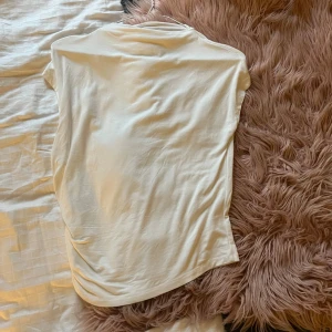 Vit t-shirt med snörning i sidan - Vit t-shirt i mjuk bomull med korta ärmar och snygg snörningsdetalj längs ena sidan. Enkel och clean design som passar perfekt till jeans eller kjol. Modellen är rak och har en lätt loose fit.  Använd en gång. 