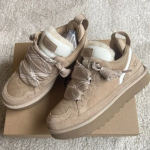 Beige sneakers från UGG med fuskpäls - Snygga beige sneakers från UGG med breda snören och fluffig fuskpäls på plösen. Skorna har en platt sula och är tillverkade i mocka och mesh med detaljer i syntet. Perfekt för dig som gillar chunky stil och vill ha något extra mjukt och bekvämt.
