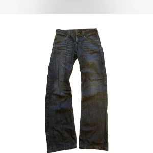 Vintage bootcut jeans - Säljer ett par mörkblå jeans med bootcut passform och coola slitningar. Jeansen har breda ben, flera fickor och kontrastsömmar. Materialet är klassisk denim och de har en avslappnad streetstil som passar perfekt till sneakers och hoodie.