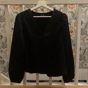 Svart v-ringad blus med långa ärmar - En svart blus från Vero Moda med v-ringning och långa ärmar. Blusen har en lätt puff vid axlarna och är tillverkad i ett mjukt tyg med diskret struktur. Perfekt för att lyfta din outfit med en stilren och enkel look, passar bra till både skolan men även finare tillställningar. Toppen är i storlek S men passar även M. Endast använd några få gånger🩷