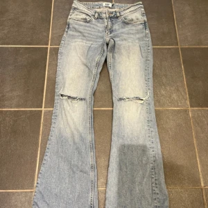Bootcut jeans från 157, ljusblå - Säljer ett par ljusblå bootcut jeans från 157 med låg midja och slitna detaljer vid knäna. Jeansen har klassisk femficksdesign, dragkedja och knapp framtill. Materialet är jeans med snygg tvättad look och lite stretch för skön passform.
