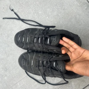 Nike Air Vapormax Plus svarta sneakers - Nike Air Vapormax Plus sneakers i helsvart färg med chunky, transparent sula och snygga vågiga detaljer på ovansidan. Skorna har snörning och är tillverkade i syntet och textil. Perfekt för dig som gillar sportig och modern stil.