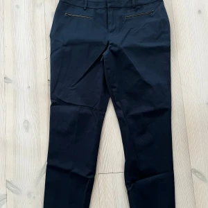 Mörkblå byxor Tommy Hilfiger stl M - Snygga mörkblå ankelkorta kostymbyxor från Tommy Hilfiger med raka ben och diskreta fickor med svarta dragkedja fram. Fint skick. Djur- och rökfritt hem. Stl M.