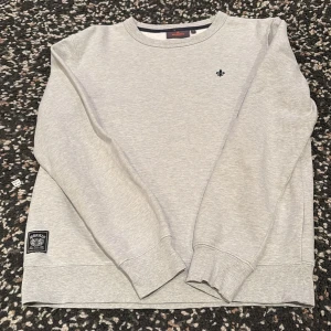 Ljusgrå sweatshirt från Morris strl S mkt fint skick  - En stilren ljusgrå sweatshirt från Morris med broderad logga på bröstet och patch vid nederkanten. Tröjan har rund hals, långa ärmar och ribbade muddar. Perfekt för dig som gillar en clean och klassisk look. Tröjan är i mkt fint skick. Strl S
