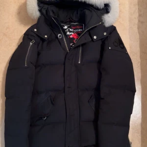 Svart 3Q Moose Knuckles vinterjacka - Säljer en svart vinterjacka från Moose Knuckles med fluffig vit päls på huvan, klassisk Moose Knuckles badge på ärmen. Jackan har använts en vinter och är i bra skick. Ny pris ligger på 14000kr. Kan även visa bild på Äkthetsbevis om ni frågar om de
