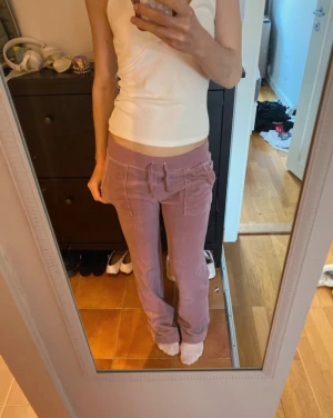 Ljuslila velourbyxor Juicy Couture XS - Säljer ett par ljuslila velourbyxor från Juicy Couture i storlek XS. Byxorna har bred resår med snörning i midjan, raka ben och fickor både fram och bak med knappdetaljer. Perfekta för en chill och trendig look. Har Knappt användt dessa så är dom helt nya!!
