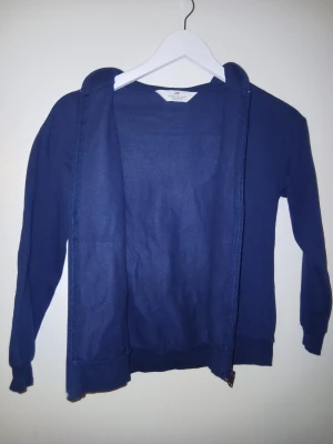 Mörkblå hoodie från H&M med dragkedja - Säljer en enkel och snygg mörkblå hoodie från H&M. Tröjan har huva, långa ärmar och praktisk dragkedja framtill. Tillverkad i mjuk bomull och har en klassisk känguruficka. Perfekt för chill dagar eller när du vill ha en casual look.