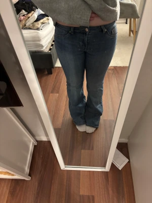 Blå bootcut jeans från H&M Divided - Snygga blå bootcut jeans från H&M Divided i storlek 38. Klassisk femficksmodell med låg midja och slitna detaljer vid bensluten för en cool vibe. Jeansen är tillverkade i jeansmaterial och har en normal passform. MIDJEMÅTT 76cm. INNERBENSLÄNGD 79cm.