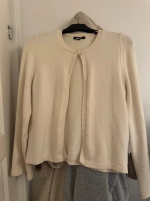 Beige kofta från Gina Tricot - Mysig beige kofta från Gina Tricot med rund halsringning och knappstängning upptill. Koftan har långa ärmar och är stickad i mjukt material, perfekt för lager-på-lager. Enkel och clean design som funkar till många olika stilar.