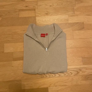 Beige half zip tröja från RYVLS - Snygg beige stickad tröja från RYVLS med half zip och hög krage. Tröjan har långa ärmar och ribbade muddar vid ärmslut och nederkant. Materialet är en skön mix av bomull och akryl, perfekt för dig som gillar stilren och enkel design. Tveka inte om att ställa frågor! 