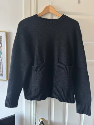 Svart stickad tröja från Zara - Bra skick, endast lite nopprig! Svart stickad tröja från Zara med rund hals och två fickor framtill. Tröjan har breda ribbade muddar vid ärmslut och nederkant, samt långärmad och loose passform. 