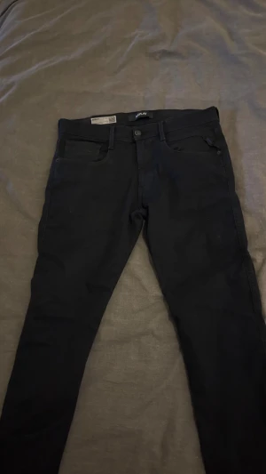 Svarta Replay Anbass jeans slim fit - Svarta Replay Anbass jeans i slim fit med klassisk femficksdesign. Jeansen är tillverkade i stretchigt Hyperflex-material som ger extra komfort och rörelsefrihet. Snygg, stilren look med svarta sömmar och diskret Replay-lapp bak i midjan.skriv gärna vid frågor. Pris kan diskuteras.