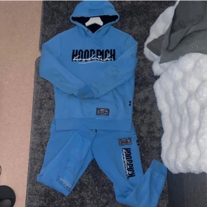 Blå hoodie från Hoodrich med brodyr - Säljer en blå hoodie från Hoodrich med broderad logga framtill och tryck på både fram- och baksida. Hoodien har huva med snörning och ribbade muddar. Perfekt för dig som gillar streetwear och vill sticka ut med en snygg och bekväm tröja.