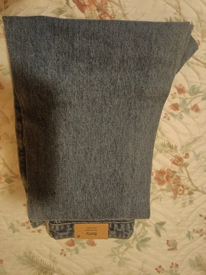 Blå raka jeans Betty från Lindex - Snygga blå jeans från Lindex, modell Betty med rak passform och hög midja. Klassisk femficksdesign, robust denim och gul kontrastsöm. Perfekta för dig som gillar en enkel och tidlös look med lite retrovibe.