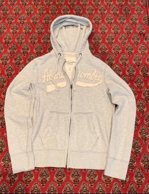 Ljusgrå hoodie Abercrombie & Fitch - Snygg ljusgrå hoodie från Abercrombie & Fitch. Storlek S, super fräsch och stilren passar till allt! Textens slitningar är design, 10/10 skick
