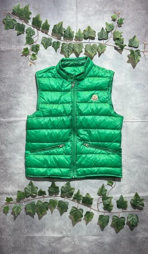 Moncler Gui Väst i Grön Storlek S (Grischelino Västen) [ÄKTA] - 🎨 Färg: Grön 📏 Storlek: Small (S) ♻️ Skick: 9/10 – inga fläckar, hål eller skador 🧵 Material: Quiltad lättviktsdunväst  ✨ Detaljer:         •        Klassisk Moncler-dunväst         •        Hög krage         •        Två snedställda framfickor med dragkedja         •        Moncler-patch på bröstet         •        Tvåvägsdragkedja framtill