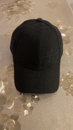 Svart Fendi keps  - Snygg svart keps från Fendi med diskret FF-logga i ton-i-ton mönster över hela kepsen. Justerbar rem bak i svart skinn med Fendi-tryck. Insidan har Fendi-loggor och etikett med 'Made in Italy'. Perfekt för dig som gillar exklusiva accessoarer. Har använt 2 gånger. Pris kan diskuteras.