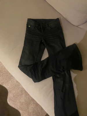 Bootcut svarta jeans från Cheap Monday - Svarta jeans från Cheap Monday i bootcut-modell. Snyggt klassiskt snitt med fem fickor och guldiga detaljer vid knappen. Jeansen är tillverkade i bomull och har en mörk tvätt som ger en cool vibe. Ganska använda men fofarande ett bra sckik 