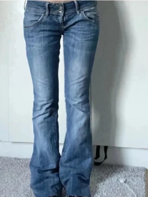 Tommy Hilfiger bootcut jeans blå - Säljer ett par blå bootcut jeans från Tommy Hilfiger med klassisk femficksdesign och låg midja. De är lite slutna nertill men inget man tänker på