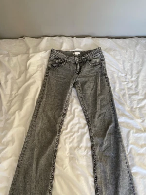 Grå bootcut jeans från Gina Tricot - Säljer ett par grå jeans från Gina Tricot med bootcut-modell. Jeansen har låg midja, dubbla knappar i linningen och klassiska fem fickor. De har en snygg tvättad look.