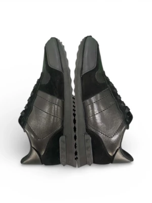 Valentino Garavani svarta sneakers - Säljer ett par svarta Valentino Garavani sneakers med coola detaljer och mattsvarta partier i skinn och mocka. Snygg kamouflagemönstrad ovandel och ikoniska nitar på sulan. Skorna har snörning och platt sula, perfekt för dig som gillar exklusiv streetstyle.