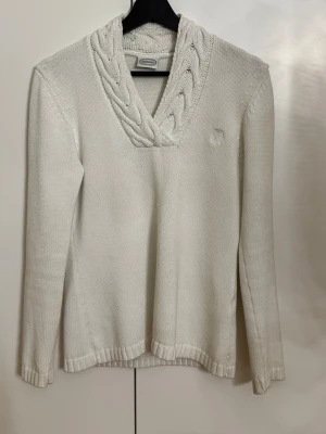 stickad tröja från det svenska kvalitetsmärket Newhouse. - Säljer en ikonisk off-white stickad tröja från Newhouse. Fantastisk kvalitet med lyxig flätstickad sjalkrage och broderad logga på bröstet. Perfekt för en chic "Old Money" eller "Quiet Luxury"-look. Upplevs som högkvalitativ bomull som håller formen perfekt. * Skick: Toppskick!  * Stil: Klassisk, feminin & sportig. *  Material: Troligtvis 100% bomull (mjuk, andas och är skön mot huden). * Nypris för liknande modeller: ca 1 500 – 1 800 kr).