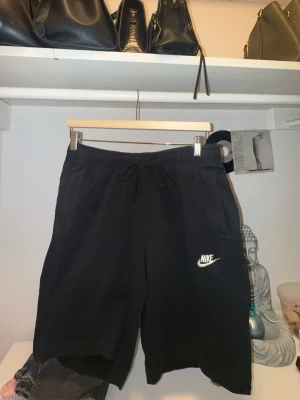 Svarta Nike shorts med snörning - Svarta shorts från Nike med klassisk logga broderad i vitt på benet. Modellen har elastisk midja med snörning och två sidofickor. Perfekta för chill dagar eller träning. Mjukt material som känns skönt mot huden, dock lite noppriga snören☺️❤️. Köparen betalar frakt