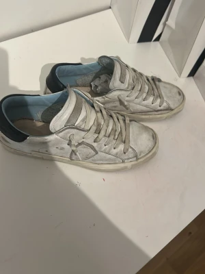 Vita Philippe Model sneakers i skinn - Säljer ett par vita Philippe Model sneakers i skinn med grå detaljer och svart häl. Skorna har klassisk snörning, ljusblå insida och en platt sula i gummi. Perfekta för dig som gillar en clean men ändå street-inspirerad look tveka inte på att skicka dm.