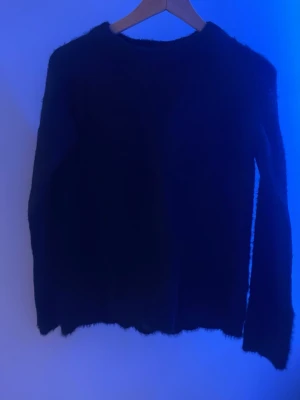 Svart fluffig stickad tröja - Mysig svart stickad tröja med lång ärm och fluffig yta. Tröjan har en enkel rund halsringning, avslappnad look. Perfekt för kyliga dagar när du vill ha något både bekvämt och snyggt. Pris går att diskuteras💗