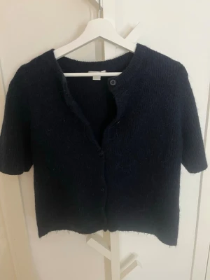 Mörkblå stickad kofta från Gina Tricot - Kortärmad, mörkblå stickad kofta från Gina Tricot. Koftan har rund halsringning, knappar framtill och är gjord i ett mjukt, fluffigt material som känns riktigt mysigt. Perfekt att slänga över en topp för en chill look. Pris går att diskutera.