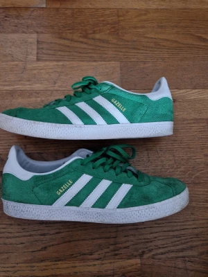 Gröna Adidas Gazelle sneakers - Säljer ett par gröna Adidas Gazelle sneakers i mocka med vita detaljer och klassiska tre ränder på sidan. 