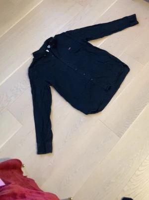 Marinblå skjorta från Levi's - Klassisk marinblå skjorta från Levi's med lång ärm och knappar framtill. Skjortan har en enkel och stilren design med liten röd Levi's-logga på bröstet. Perfekt till jeans eller chinos för en clean look.