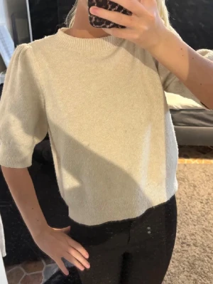 Beige stickad tröja med puffärm - Superfin beige stickad tröja med korta puffärmar och ribbade kanter. Tröjan har en rund halsringning och är lite boxig i modellen, vilket ger en chill och trendig vibe. Perfekt att styla med både jeans och kjol. Lite nopprig (se bild).