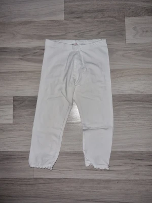 Vita 3/4 leggings från H&M med spetskant - Säljer ett par vita 3/4 leggings från H&M i storlek 122. Byxorna har en mjuk resår i midjan och söt spetskant längst ner vid bensluten. Perfekta till vardags eller när du vill ha något bekvämt och enkelt.