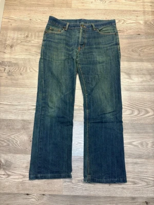 Blå jeans från Divided by H&M, 34/34 - Säljer ett par klassiska blå jeans från Divided by H&M i modellen Low Cut. Jeansen har fem fickor, orangea sömmar och är tillverkade av 85% bomull och 15% polyester. Passformen är rak med låg midja och de har en enkel, tidlös look.