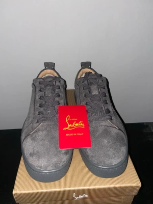 Grå mockasneakers från  Louboutin - Snygga grå sneakers i mocka från Louboutin med klassisk röd sula och diskret snörning. Skorna har en rund tå och platt sula, samt lyxig känsla med beige innersida. Perfekta för dig som vill sticka ut med exklusiva detaljer.    SAMMA PAR SOM ANDRA ANNONSEN PÅ MIN PROFIL KOLLA DÄR FÖR MER BILDER!!