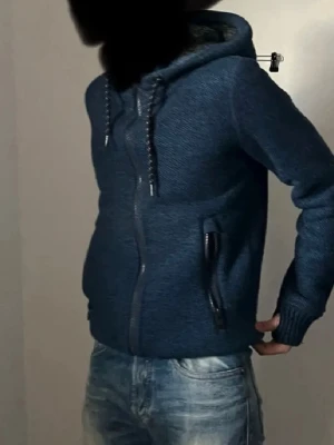 Blå hoodie, Superdry  - Säljer en blå mysig stickad hoodie från Superdry. Aldrig sett någon annan ha denna,  unik, varm och köpt från superdry i Mall of scandinavia, finns ingen superdry butik kvar i Sverige. Storlek XS, den är ganska tight och passar bra om du är lång och smal. 