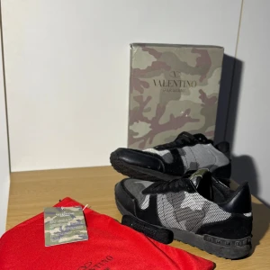 Valentino Garavani Rockrunner sneakers - Snygga Valentino Garavani Rockrunner sneakers i svart, grått och vitt med camouflagemönster. Skorna har mesh och mockadetaljer, svarta snören och en robust sula med nitar på hälen. Perfekta för dig som vill sticka ut med exklusiva och trendiga sneakers. storlek 44 passar även 43. Perfekta nu inför vintern❄️ Frågor om kvitto eller annat besvarar vi pv‼️Pris kan diskuteras vid snabb affär✅