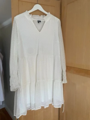 Vit prickig kortklänning Vero Moda - Supersöt vit kortklänning från Vero Moda med diskret prickigt mönster och volangdetaljer. Klänningen har långärmade transparenta ärmar med smock vid handlederna, v-ringning och ett knytband i midjan! Perfekt till studenten eller midsommar🫶(lite missfärgning men inget som syns tydligt)