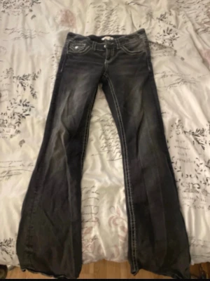 Mörka bootcut jeans lågmidjade - Säljer ett par mörkblå jeans med bootcut-modell och tydliga kontrastsömmar. Byxorna har klassisk femficksdesign och en lätt tvättad look. Perfekta för dig som gillar retrovibbar och vill ha ett par jeans som sticker ut lite extra.