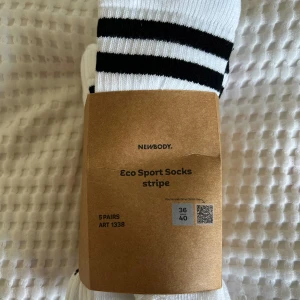 Randiga sportstrumpor från Newbody - Säljer ett 5-pack vita sportstrumpor från Newbody med svarta ränder upptill. Strumporna är ribbade och tillverkade av 70% ekologisk bomull, 28% polyamid och 2% elastan. Perfekta för dig som gillar en klassisk och sportig look.