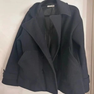 Mörkblå skepparkavaj med stora slag - Stilren mörkblå skepparkavaj från Design by si med stora slag, dubbelknäppning och två rejäla fickor framtill. Jackan har en klassisk, lite boxig passform och är fodrad för extra komfort. Perfekt för dig som gillar en tidlös look.