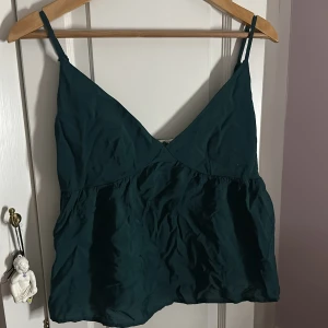 Mörkgrön linnetopp med v-ringning - Snygg mörkgrön linnetopp med smala axelband och v-ringad fram. Toppen har en lätt rynkad nederdel och dragkedja i sidan för enkel påklädning. Jättesöööt, bara inte min färg 💗 använt endast vid köp‼️