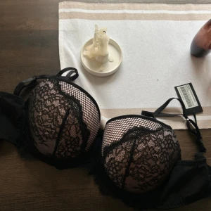 Svart spets bh Pour Moi - Säljer en snygg svart bh från Pour Moi, modell Dark Romance. Den har vadderade kupor med blommig spets och nät, samt fina detaljer längs kanterna. Axelbandslös design med justerbara band och hakknäppning bak. Färgen är svart med rosa underton.