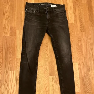Svarta jeans Calvin Klein - Svarta jeans från Calvin Klein Jeans med passform. Klassisk femficksdesign, dragkedja och knapp framtill. Jeansen har en mörk tvätt med lätt slitning och är tillverkade i stretchigt jeansmaterial för en tajt look. Nypris: 1500 Mitt pris 450
